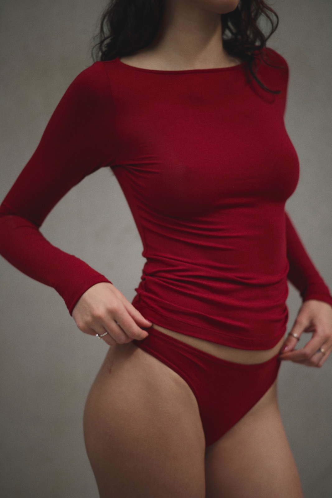 Katja hitching a red long sleeve top at the hip against concrete, photographed by Eli Samuel for Australian Stitch.