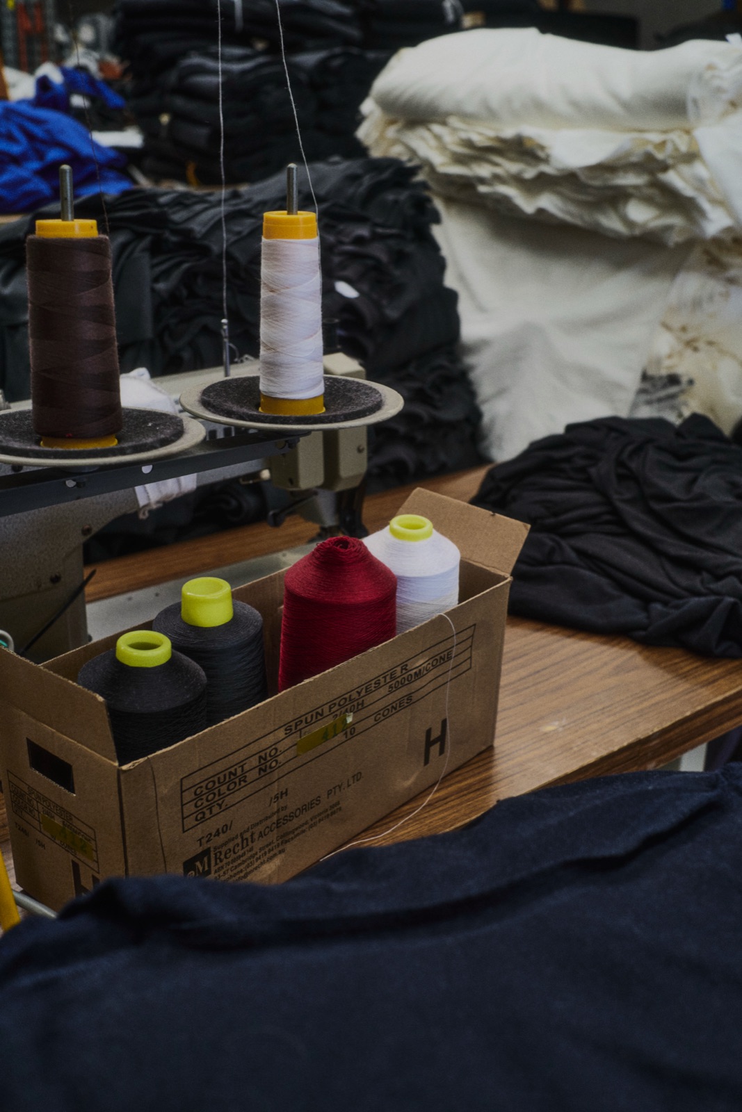 Reels of thread in a cardboard box among stacked fabric, photographed by Eli Samuel for Australian Stitch.