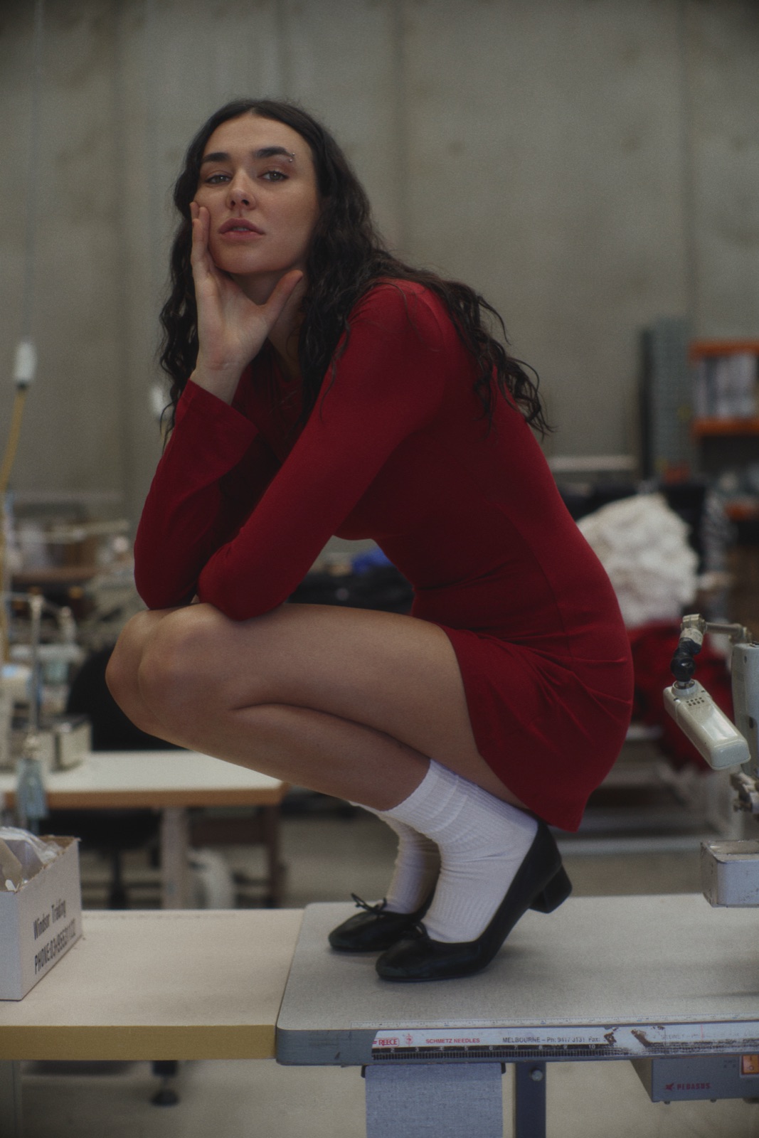 Katja crouching on a sewing table in a red dress and white socks, photographed by Eli Samuel for Australian Stitch.