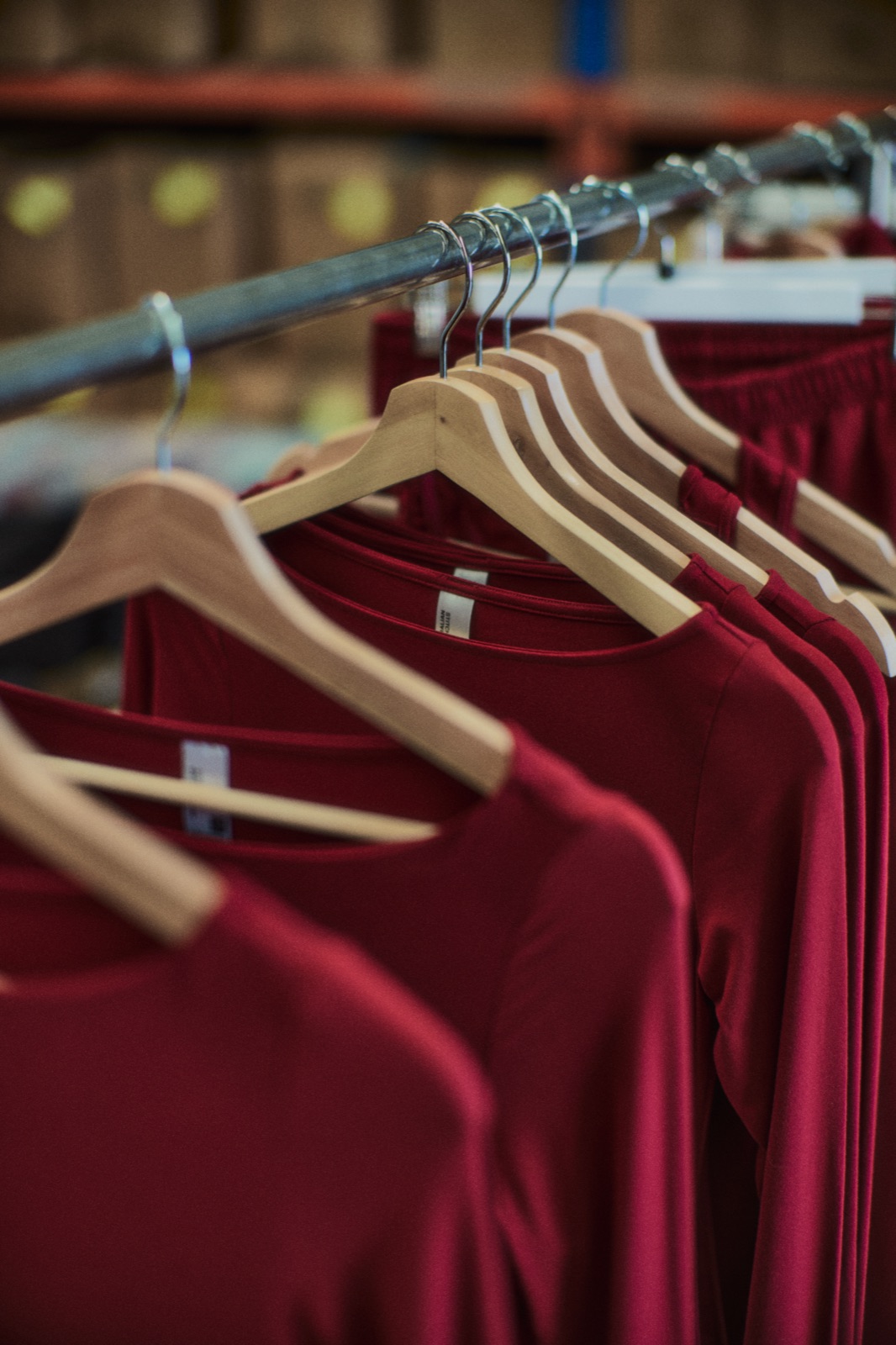 Red garments on wooden hangers on a factory rail, photographed by Eli Samuel for Australian Stitch.