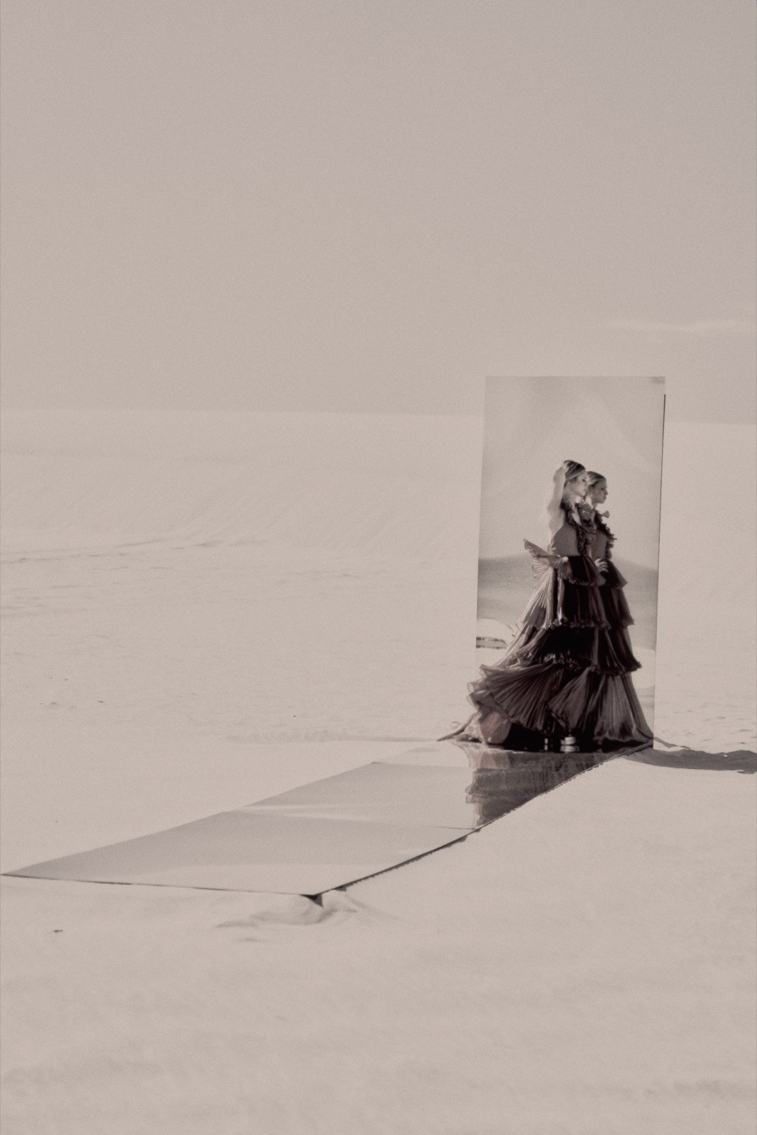A model in a ruffled gown reflected in a mirror on the white sand, photographed by Eli Samuel for Sherri Hill.