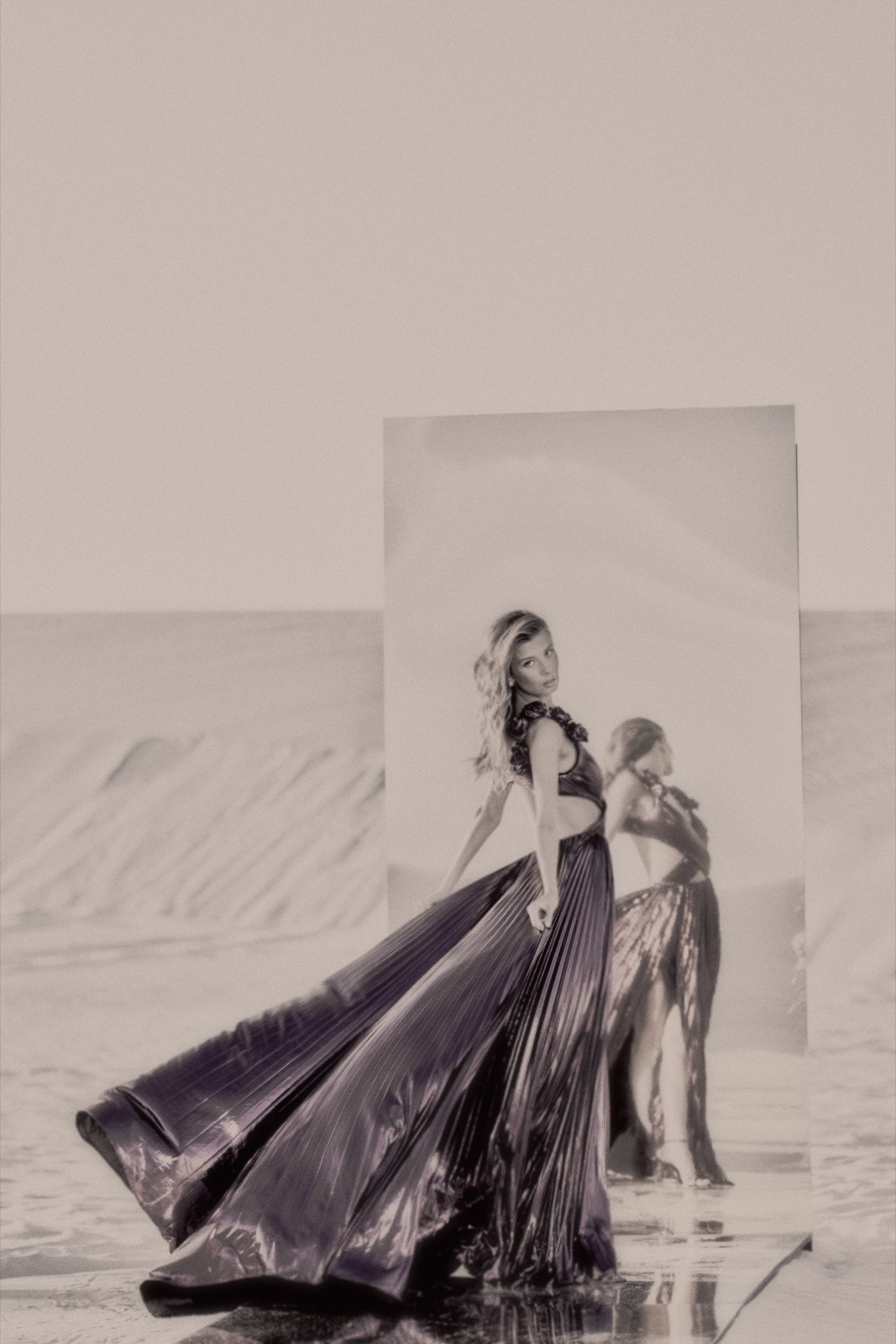 A model in a pleated metallic gown caught mid-stride, reflected beside her, photographed by Eli Samuel for Sherri Hill.