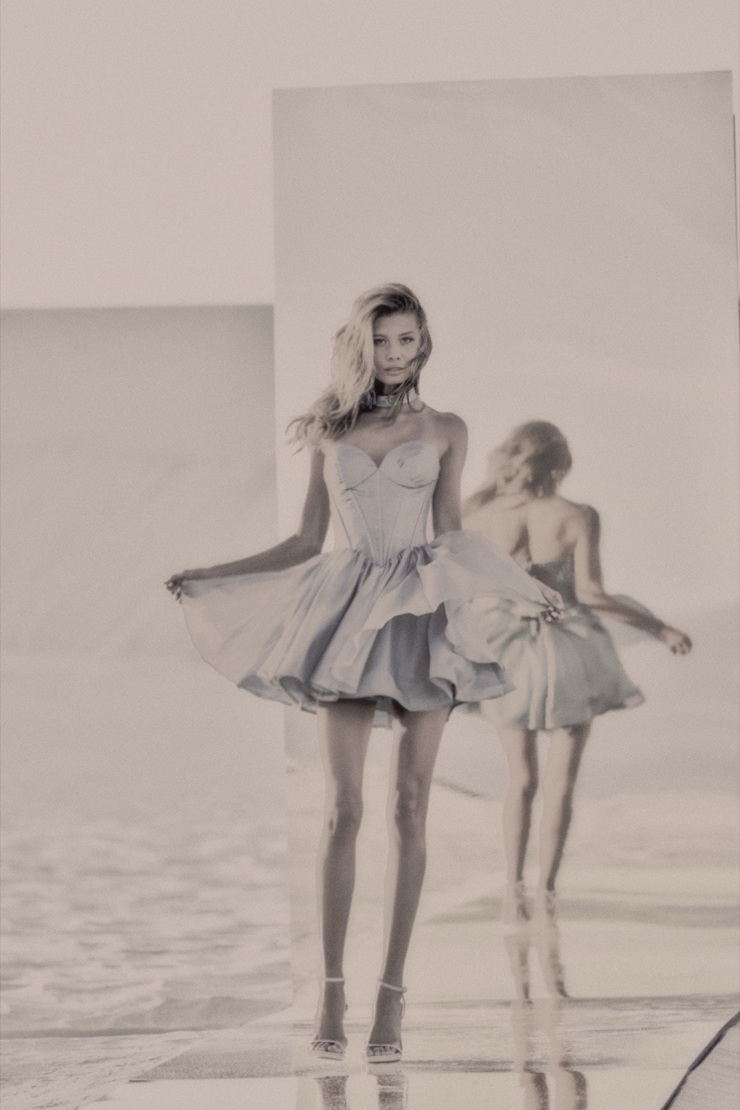 A model in a pale blue tulle dress twirling on the beach, reflected in a mirror, photographed by Eli Samuel for Sherri Hill.