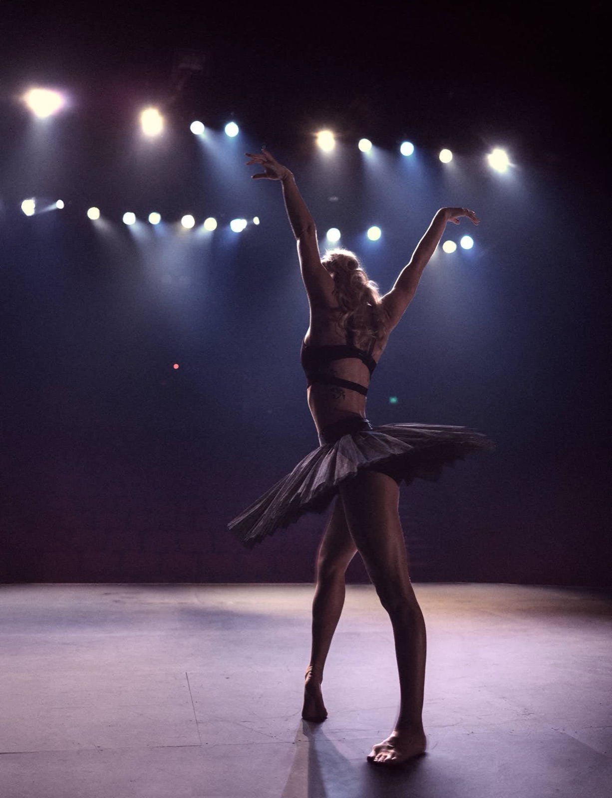 Ballerina in silhouette on stage, arms raised under stage lights