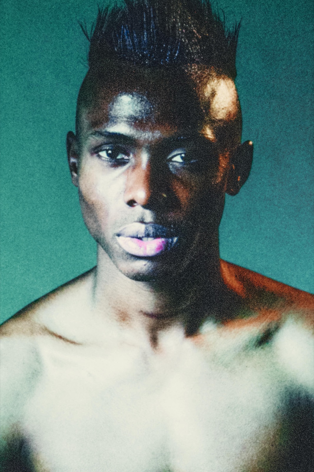 Model Déji Saka's face under teal studio light, paint on his skin, June 2014, photographed by Eli Samuel.
