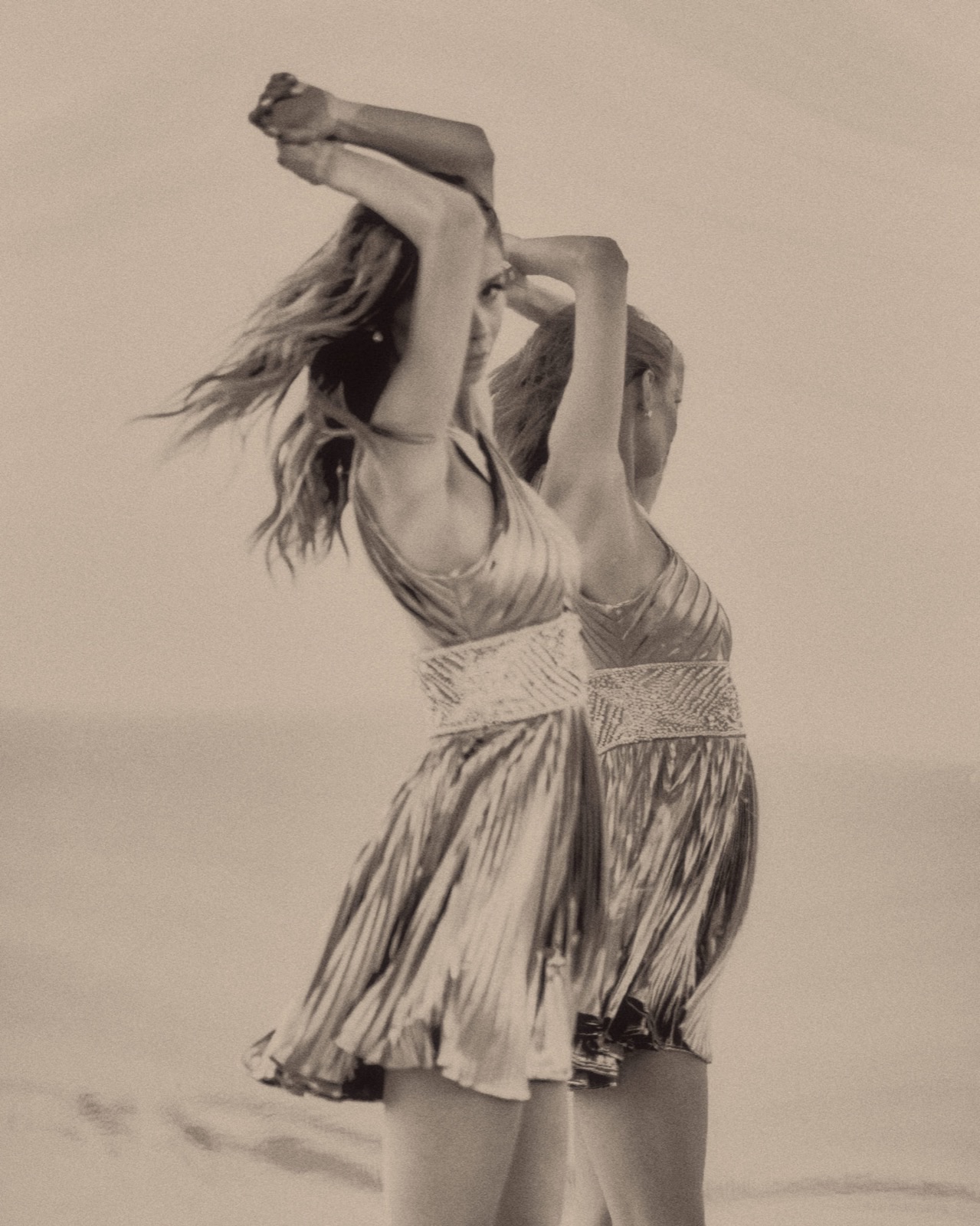 Model Fiona Briseno in a metallic pleated dress for Sherri Hill, arms raised in a double-exposed shot at El Castillo de Arena Beach, Baja California Sur, Mexico, May 2, 2024, photographed by Eli Samuel.