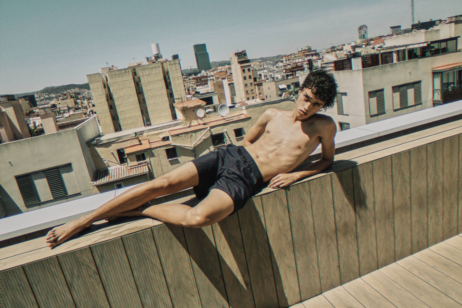Model Mario Volpi resting on a Barcelona rooftop against the sky, Summer 2026, photographed by Eli Samuel for Verano.